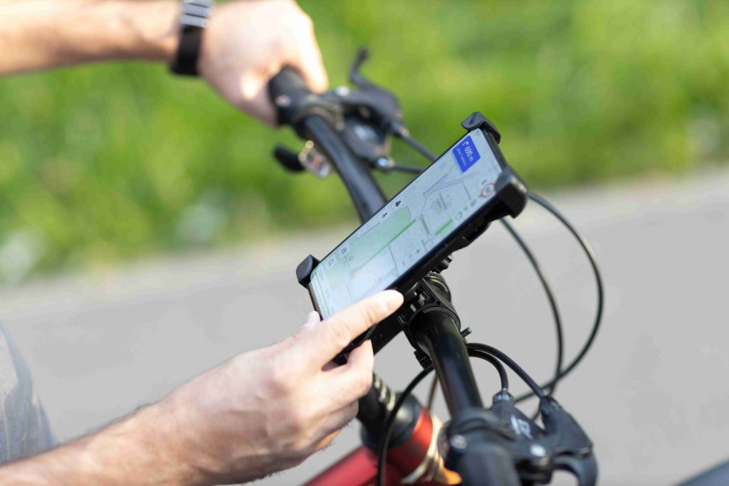 A cyclist's hands touching a smartphone screen mounted on a bicycle handlebar phone holder during an outdoor ride