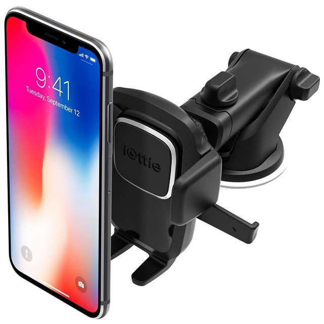 A black suction cup car phone holder with a telescopic arm standing next to a smartphone with screen turned on, isolated on a white background