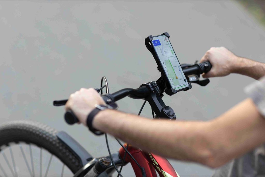 A cyclist riding a bicycle while holding the handlebars with a smartphone mounted on the center stem showing a GPS map